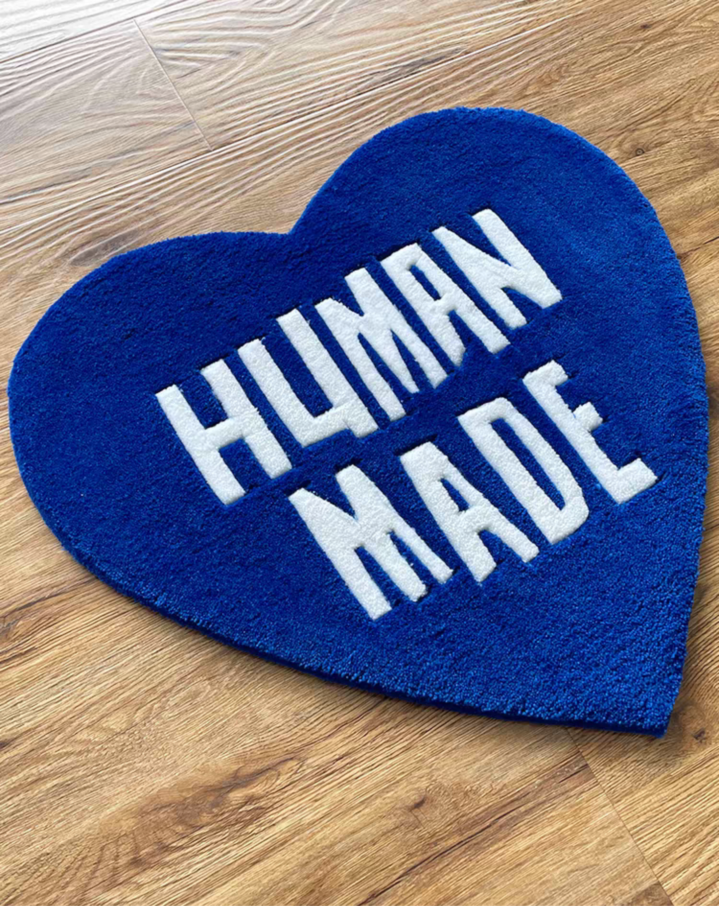 Human Made blue heart rug on wooden floor in bedroom. Handmade blue white tufted heart carpet. Sneakerhead hypebeast streetwear room floor decor.