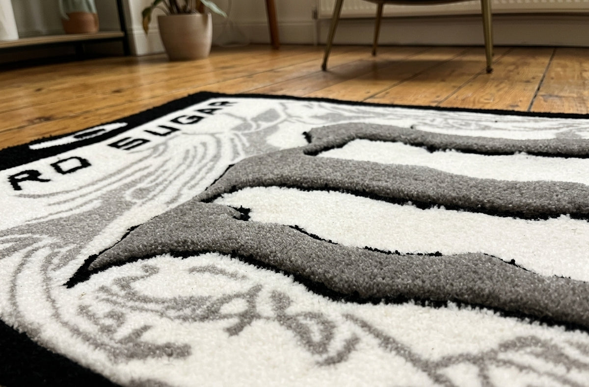 White Monster Rug close up of the grey claw mark logo in hand tufted acrylic yarn on a wooden floor