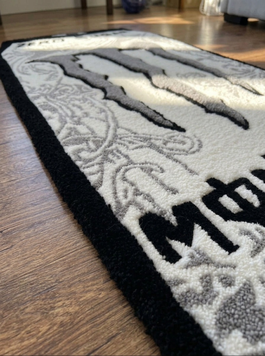 Hand tufted energy drink can rug with black border, angled close up of claw logo and lettering on a wooden floor