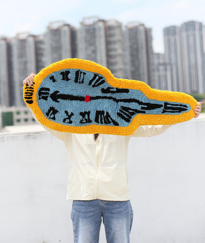 Melting clock rug held up to show the drooping abstract shape, soft high-density acrylic yarn