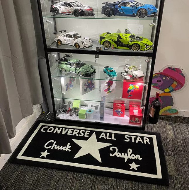 Display case with model cars on a carpeted floor featuring a Converse All Star rug.