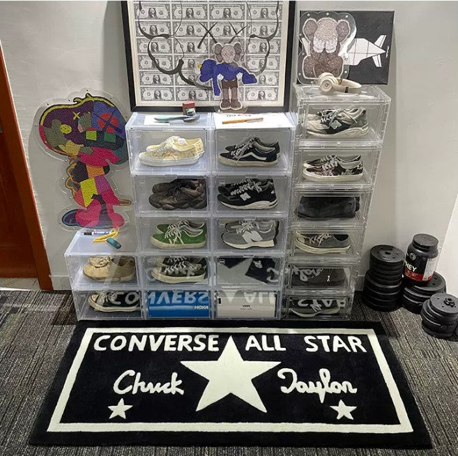 Clear shoe storage boxes with various shoes inside, placed on a carpeted floor with a Converse All Star rug.