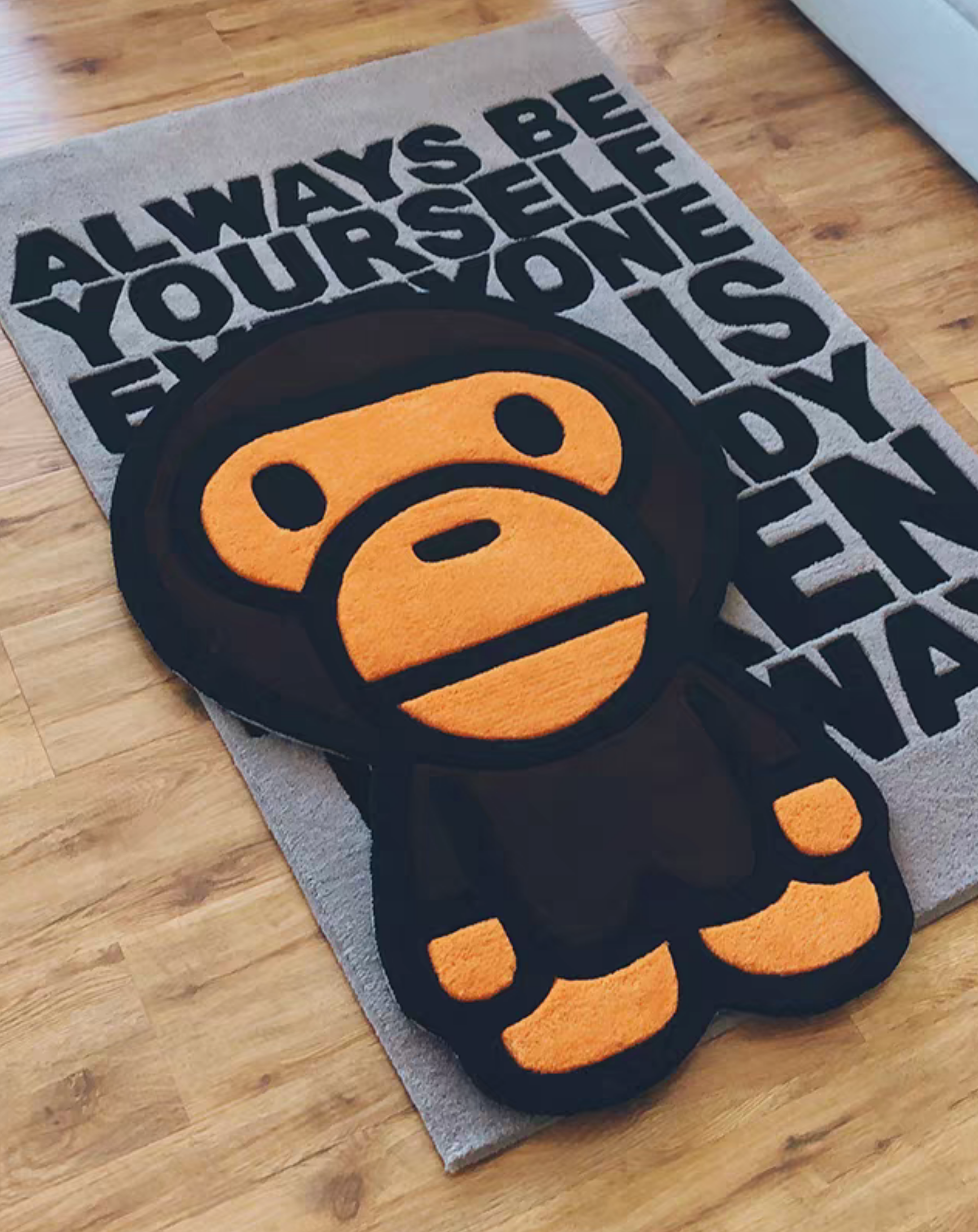 Baby Milo Bape rug on wooden floor in bedroom. Handmade orange brown black tufted Ape Head carpet. Sneakerhead hypebeast streetwear room floor decor.