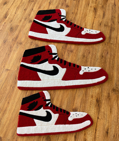 Three sizes of the red sneaker rug lined up on a wood floor, size comparison view
