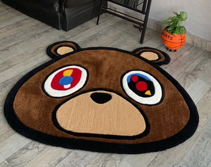 Kanye Dropout Bear Rug Close Up, bear-shaped area rug with a cartoon bear face design, placed on a light gray wood-look floor in a room setting.