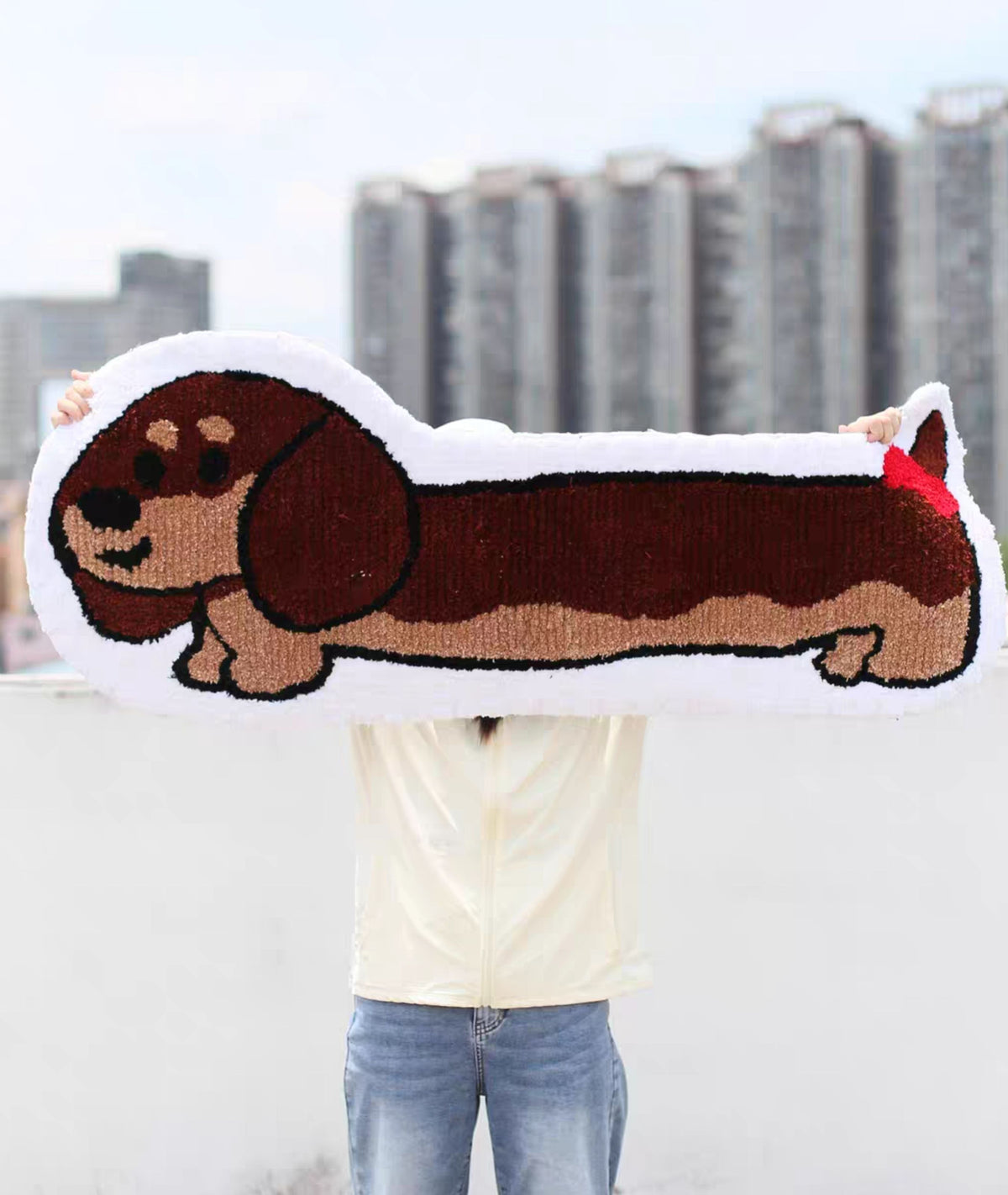 Person holding the long dog rug outdoors, size scale for the hand tufted dachshund design