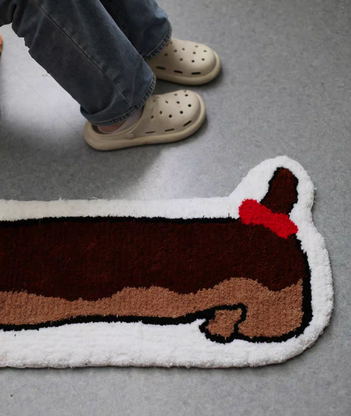 Long dog rug with a small red bow beside a person standing, scale and shape on the floor