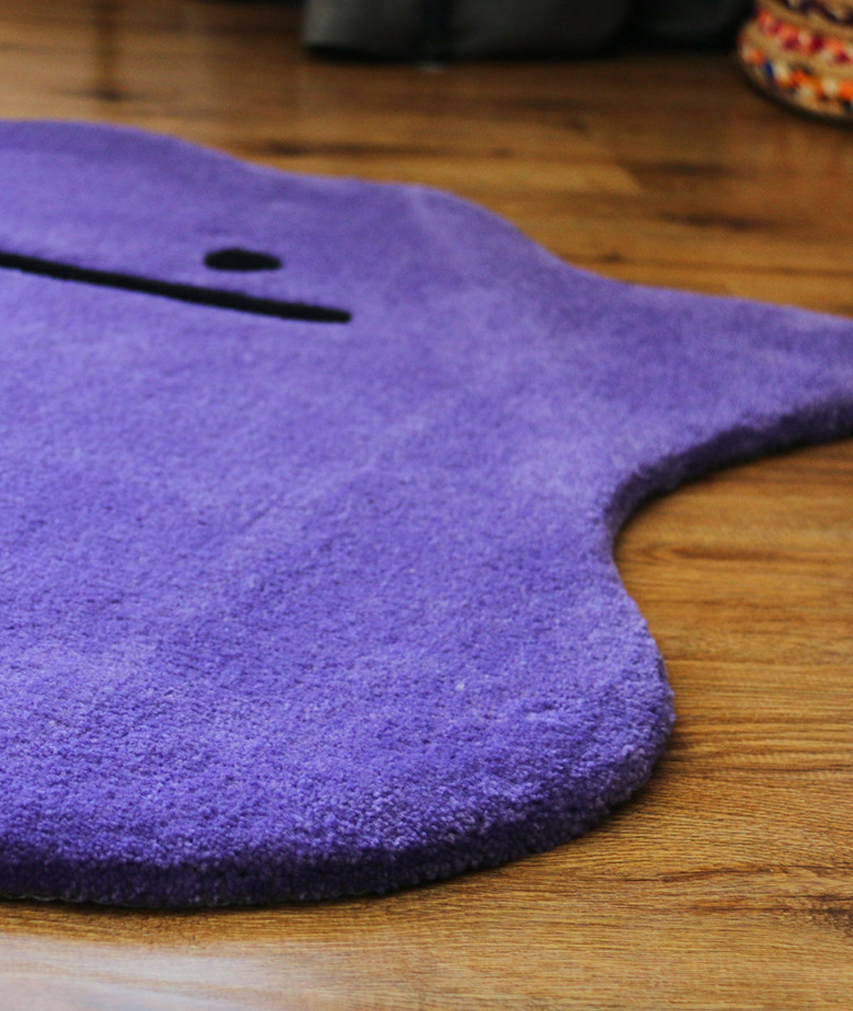 Shaped purple area rug edge on hardwood, plush acrylic yarn surface, low angle corner view