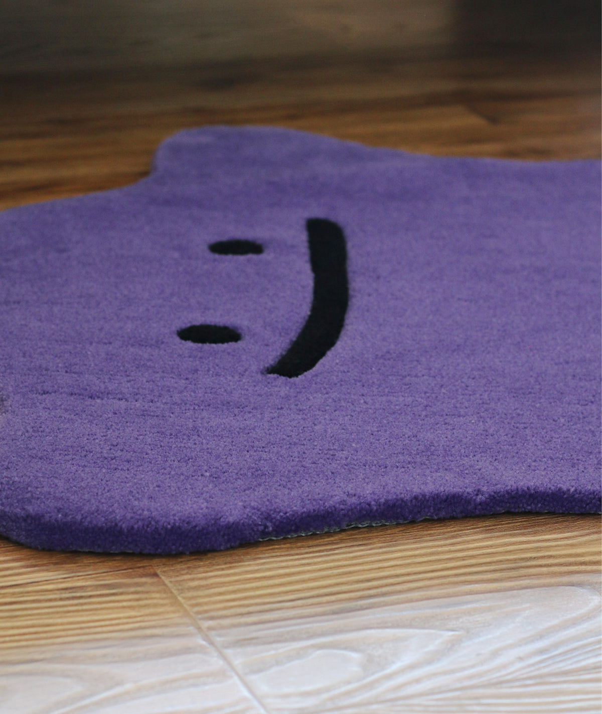 Close up of the purple rug face, black stitched eyes and mouth on dense pile, detail view