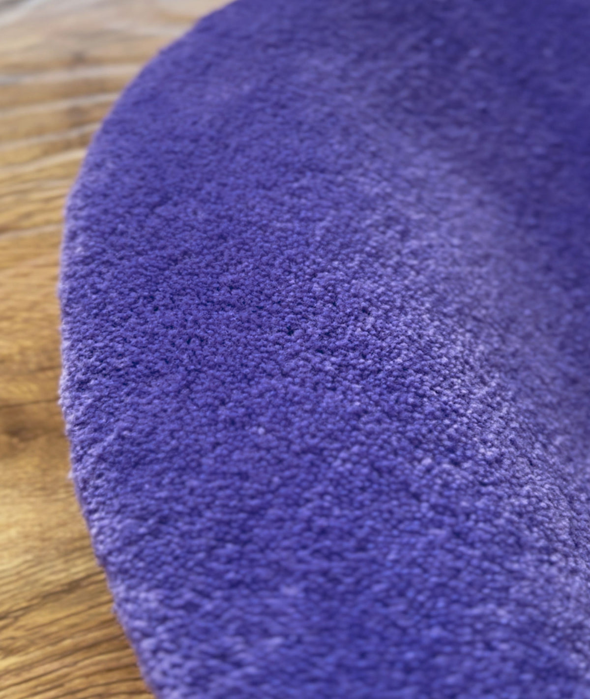 Macro shot of purple rug pile, dense looped acrylic yarn texture on a wood floor