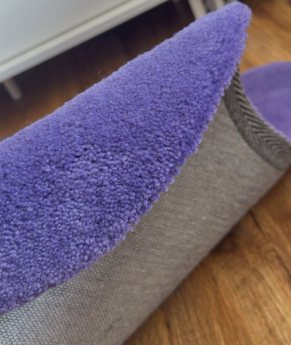 Underside of the purple rug showing the grey non slip backing, edge folded over on wood