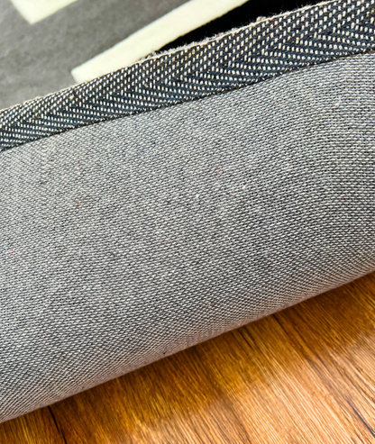 Underside of the flag rug rolled back, grey woven non slip backing on a wood floor