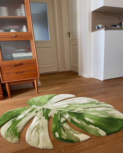 A large monstera leaf-shaped area rug in green and cream is placed on a wooden floor in a modern living room setting.
