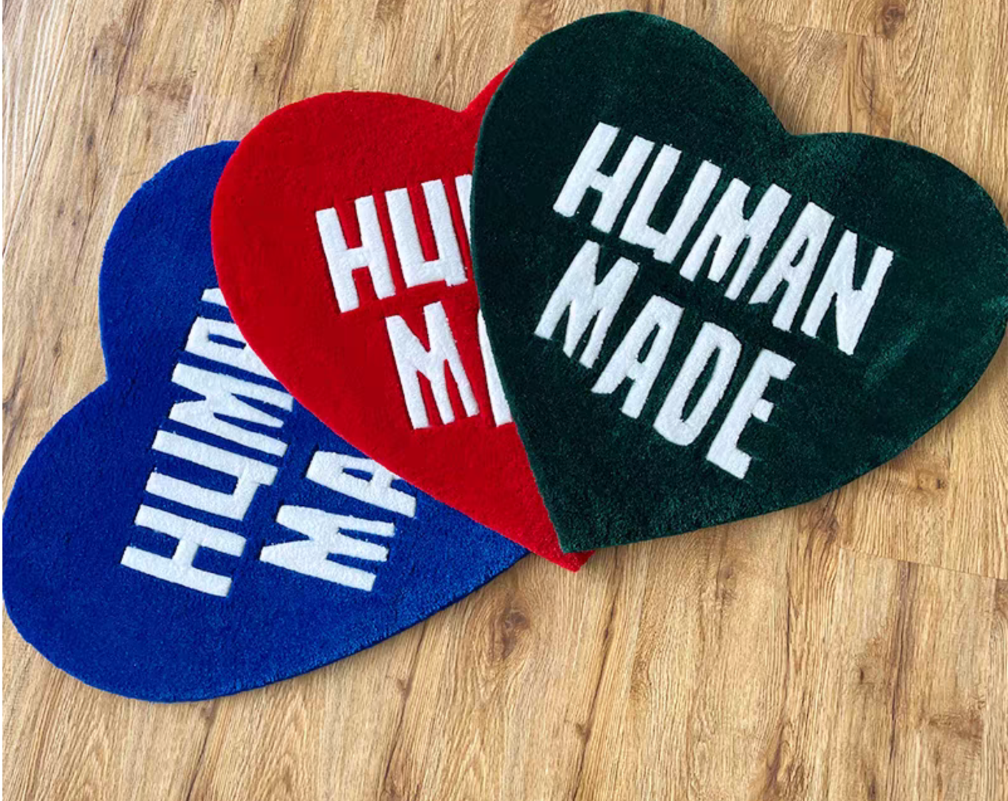 Human Made green red blue heart rugs on wooden floor in bedroom. Handmade tufted heart carpet collection. Sneakerhead hypebeast streetwear room floor decor set.