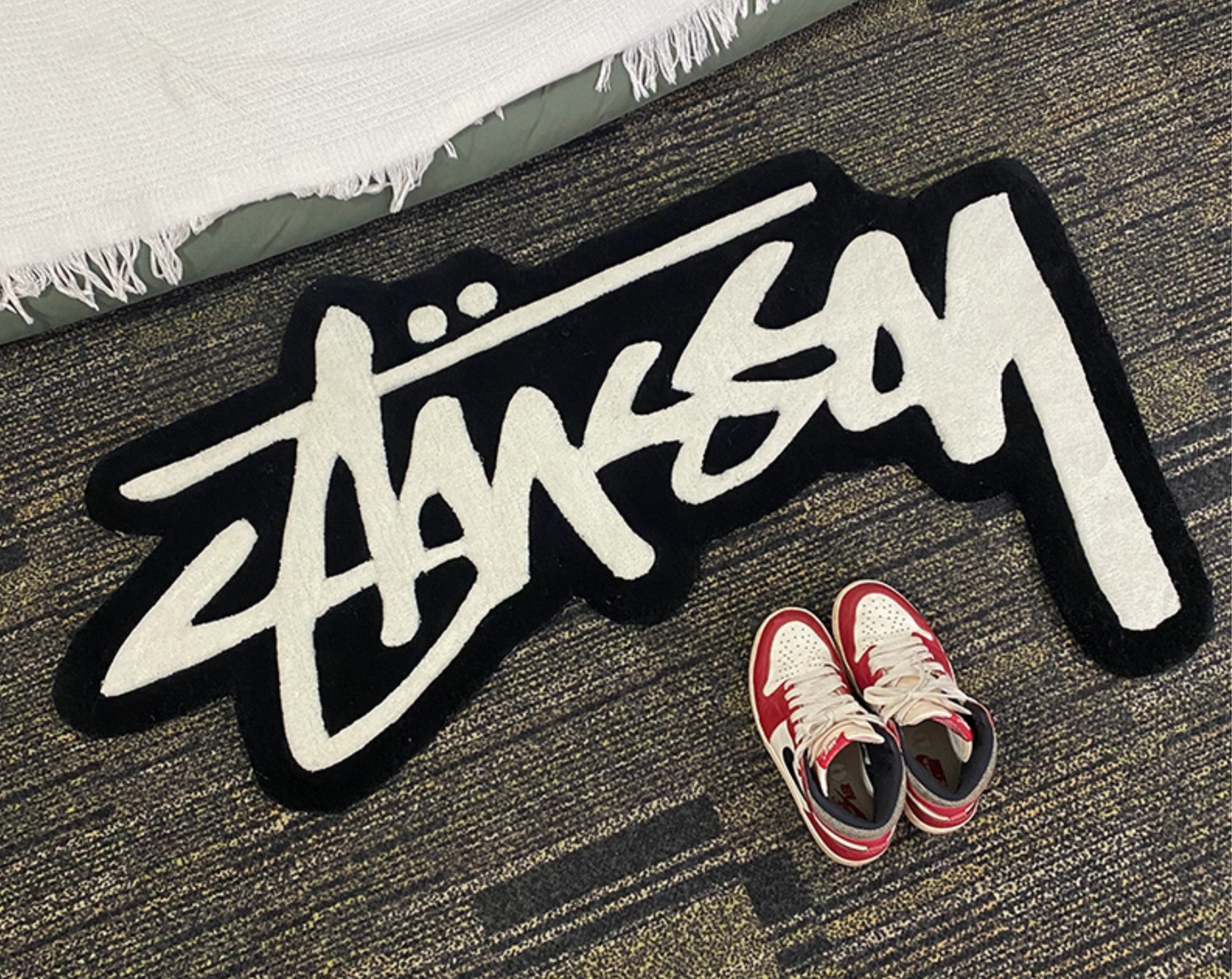 Streetwear graffiti script tufted rug black and white styled next to Air Jordan 1 sneakers, hypebeast bedroom rug with shaped cut edges, sneaker display rug for clothing room or sneakerhead setup