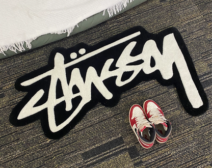 Streetwear graffiti script tufted rug black and white styled next to Air Jordan 1 sneakers, hypebeast bedroom rug with shaped cut edges, sneaker display rug for clothing room or sneakerhead setup