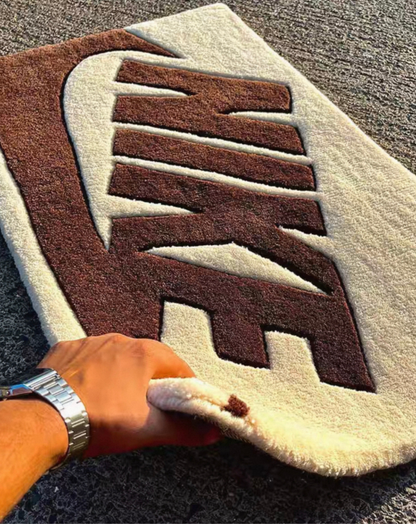 Brown cream swoosh tufted rug flat lay, sneakerhead clothing room decor rug, bold logo bedroom rug for streetwear and sneaker culture enthusiasts