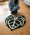 Monstera leaf rug in black and white on a wood floor, hand tufted plant room decor, top view