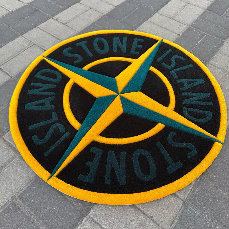 A circular Stone Island logo mat in black, yellow, and teal, placed on gray paving stones.