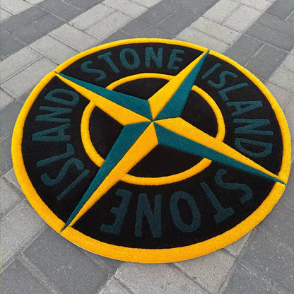 A circular Stone Island logo mat in black, yellow, and teal, placed on gray paving stones.