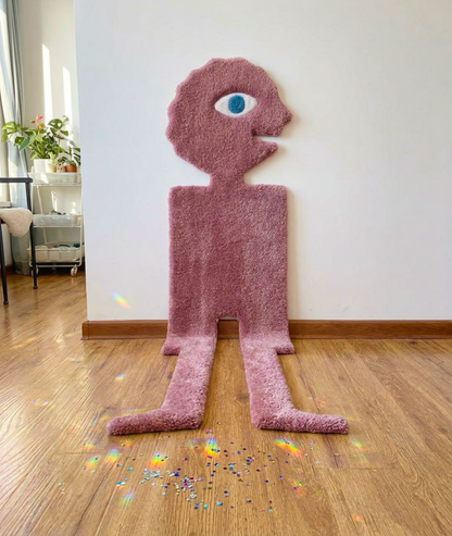 Pink one eyed monster rug standing against a wall, hand tufted cartoon room decor, full front view