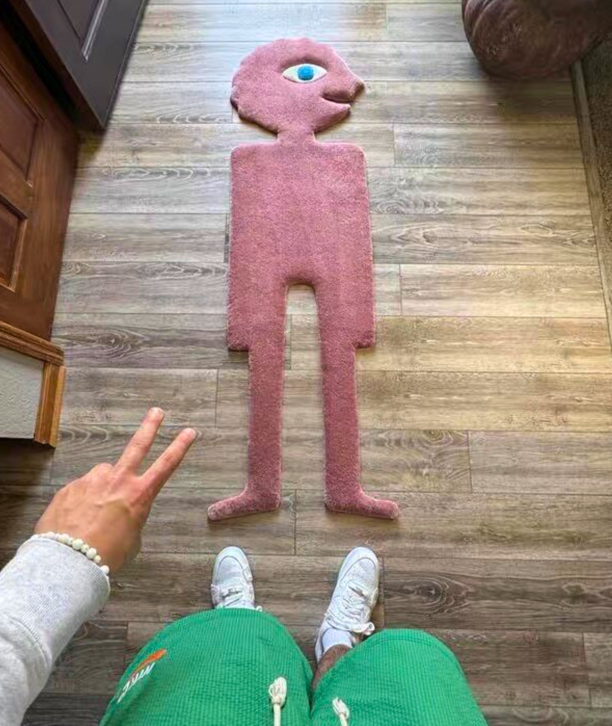 Pink monster shaped area rug seen from above next to a person, size scale on a wood floor