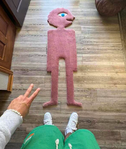 Pink monster shaped area rug seen from above next to a person, size scale on a wood floor