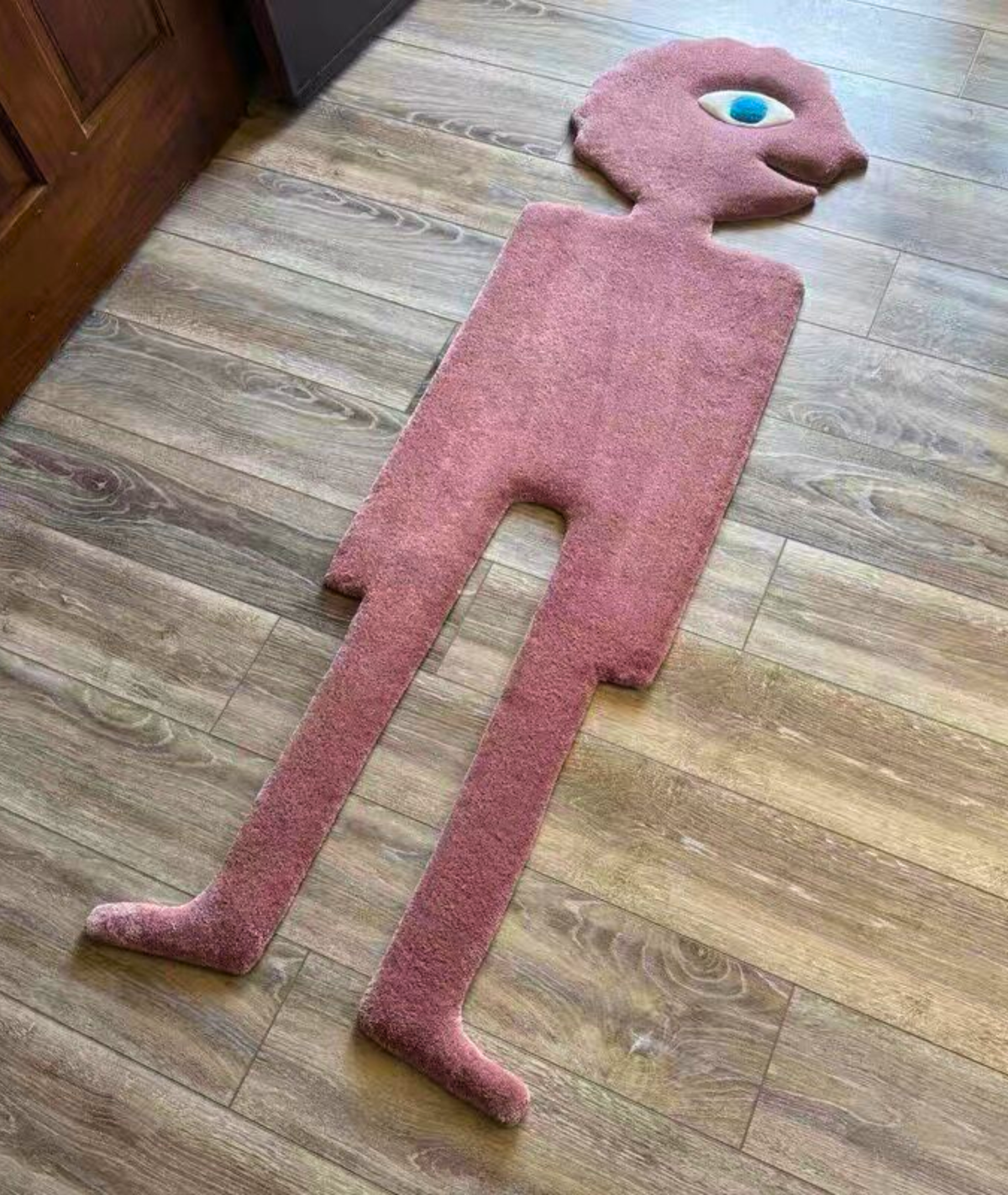 Hand tufted pink figure rug with a blue eye, dense acrylic yarn pile, angled floor view