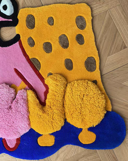 A colorful, plush, high-pile shag rug featuring a stylized cartoon design resembling SpongeBob SquarePants, with yellow, pink, blue, and brown elements, laid out on a light wood parquet floor.
