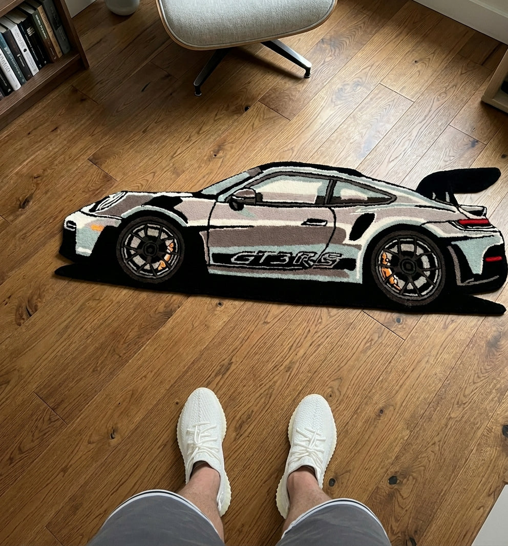 Car shaped rug in silver, grey and black with gold brakes and rear wing, standing view next to sneakers