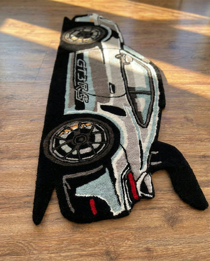 Hand tufted car rug detail of silver body, black wheels and red taillights on a wooden floor