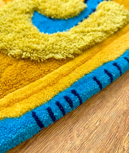 Hand tufted shoe rug close up, shaggy yellow pile over a blue sole edge, pile texture detail